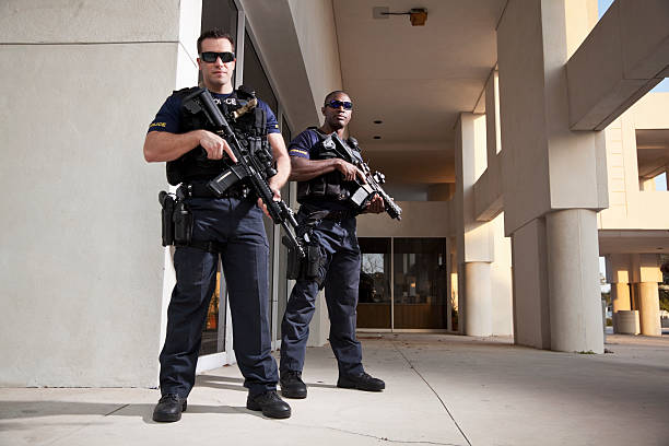 Home multi ethnic police officers (20s) wearing bulletproof vests, holding rifles.